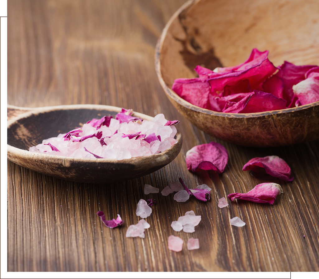 Wooden bowls with pink salt and dried rose petals on a table.