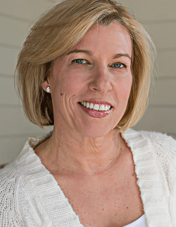 Smiling woman with short blonde hair in a cozy white sweater.