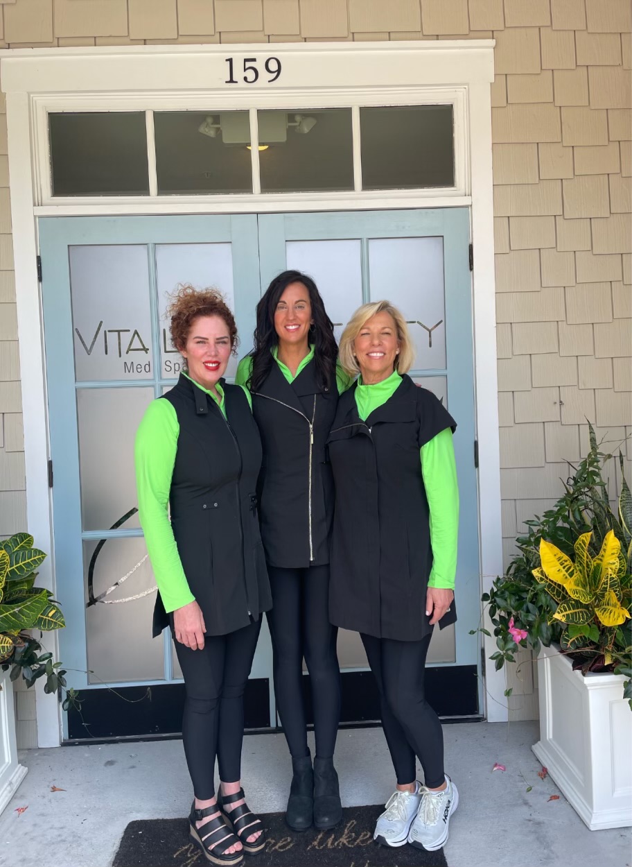 Three women standing together outside a building entrance, smiling.